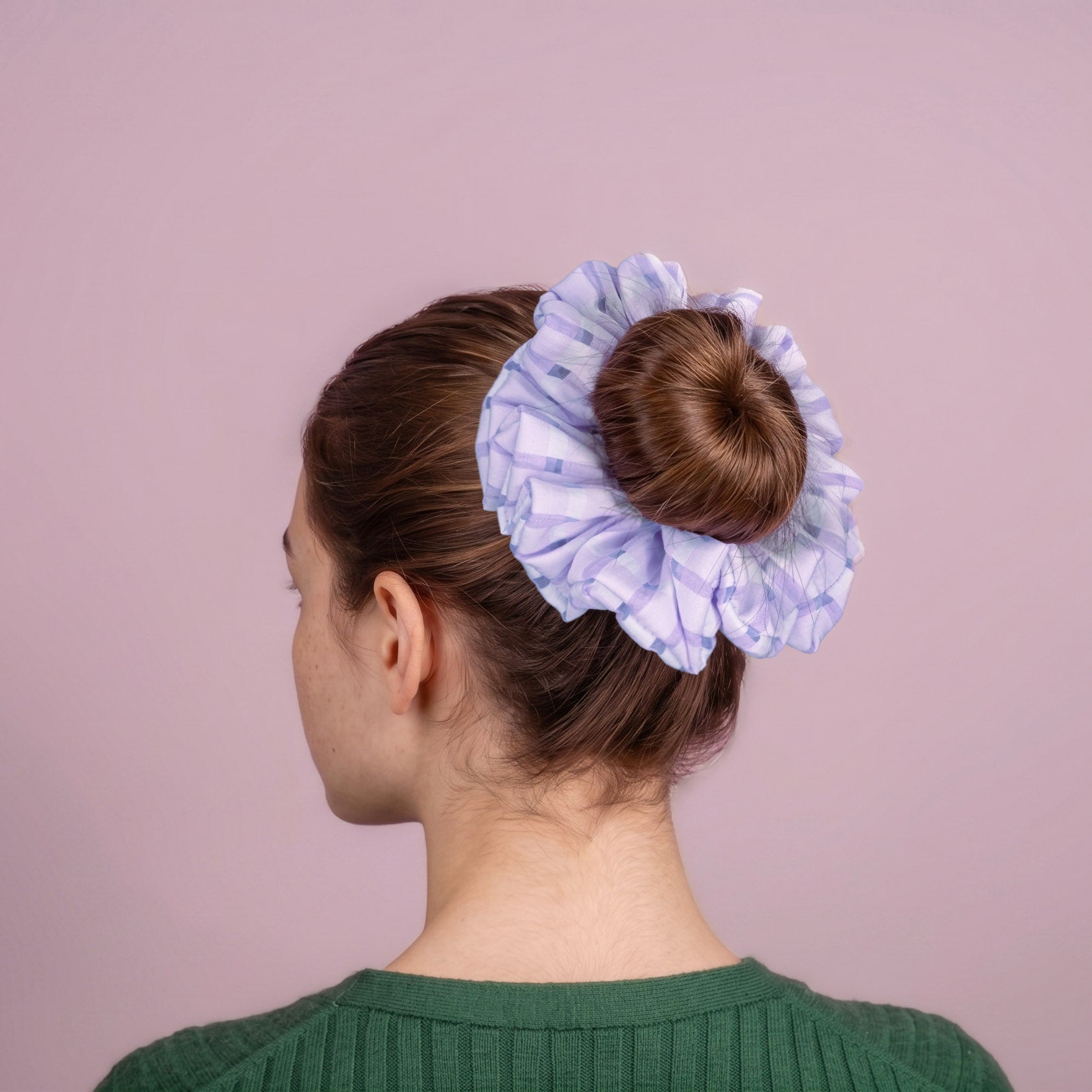 Person with a bun held by a purple organza scrunchie against a pink background