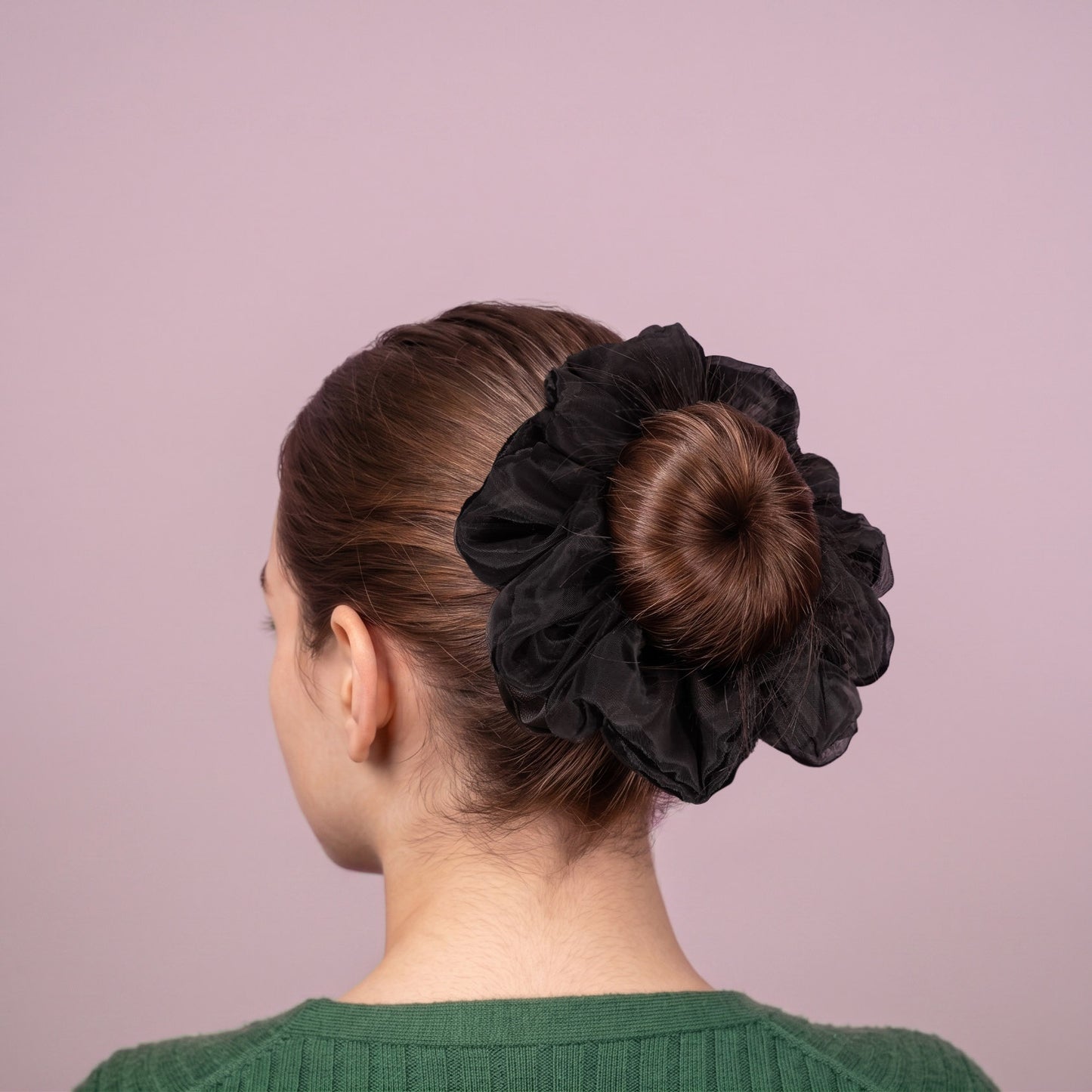 Woman with a black organza scrunchie in her hair against a pink background