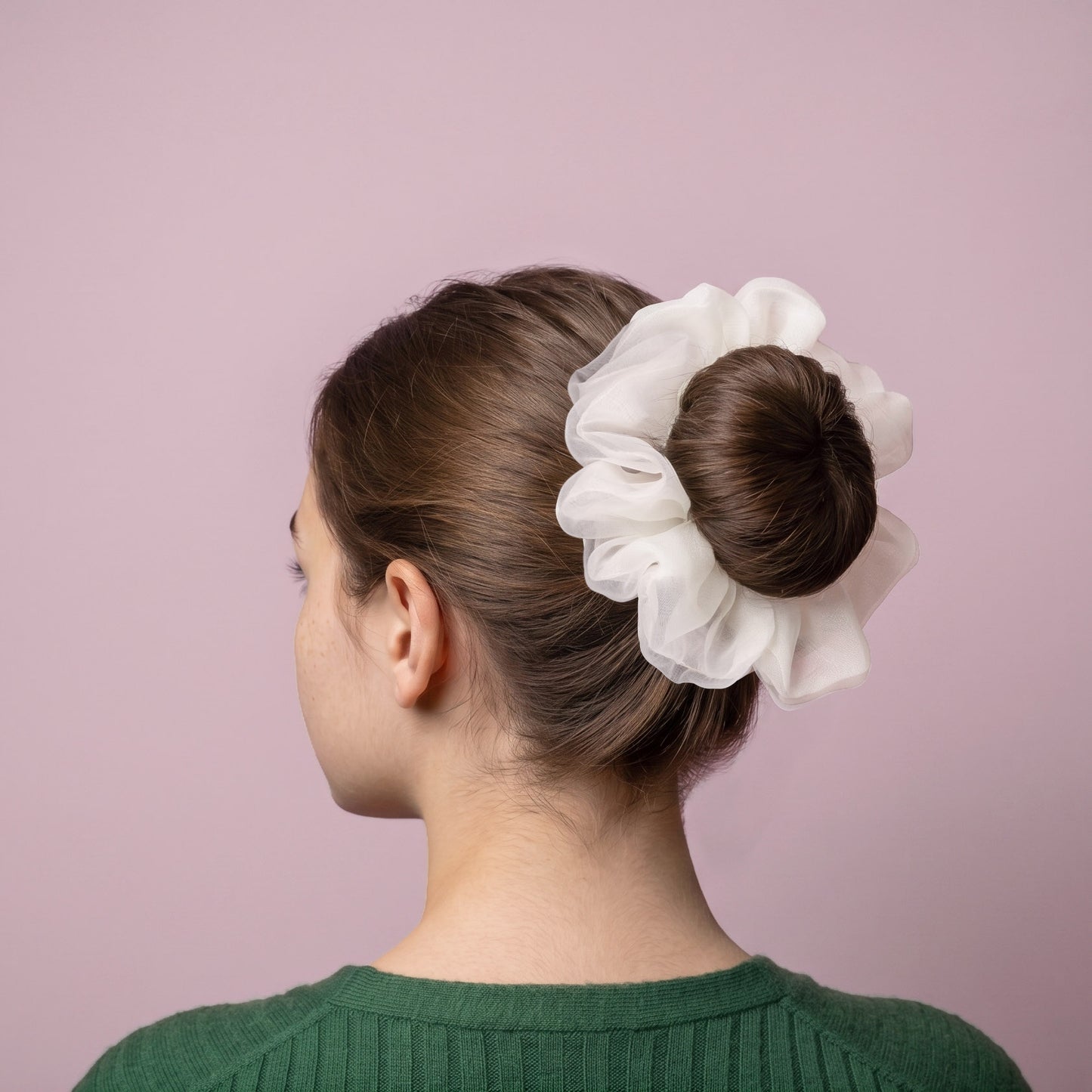 Woman with a white organza scrunchie in her hair against a pink background